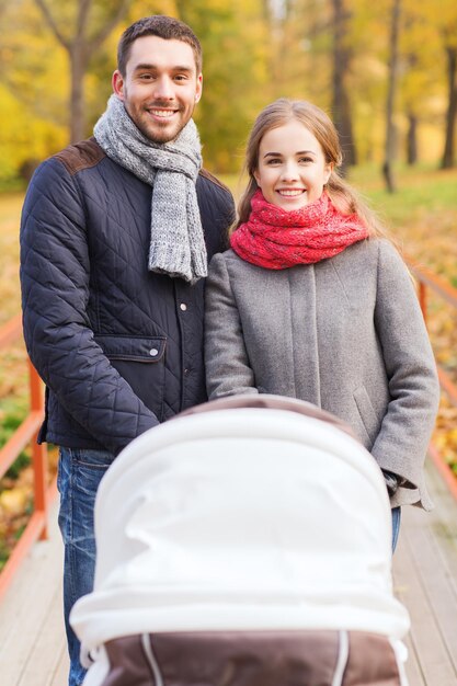 Liebe, Elternschaft, Familie, Jahreszeit und Personenkonzept - lächelndes Paar mit Kinderwagen im Herbstpark