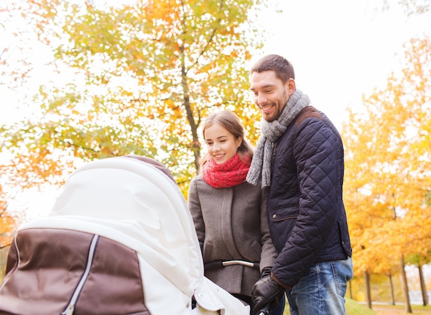 Liebe, Elternschaft, Familie, Jahreszeit und Personenkonzept - lächelndes Paar mit Kinderwagen im Herbstpark