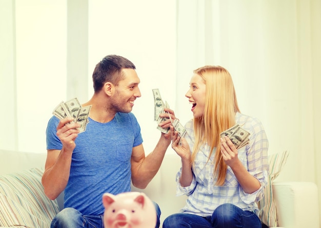 Liebe, Familie, Finanzen, Geld und Glückskonzept - lächelndes Paar mit Geld und Sparschwein am Tisch zu Hause
