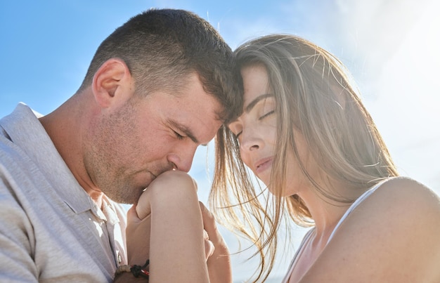 Liebe Hand und Paar küssen sich an einem Strand, der einen intimen Moment der Romantik bei Sonnenaufgang vor blauem Himmelshintergrund teilt Reisefreiheit und Mann mit Frau umarmen sich und entspannen sich in der Natur zusammen Mockup