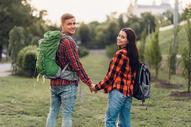 Liebe Paar Touristen mit Rucksäcken Händchen haltend, schöne Ferien. Sommerabenteuer des jungen Mannes und der jungen Frau, die im Stadtpark gehen