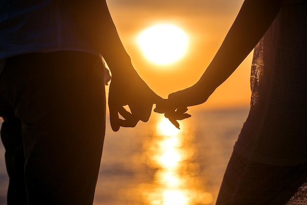 Liebe - romantisches Paarhändchenhalten, Strandsonnenuntergang. Liebhaber oder frisch verheiratetes junges Paar in Romantik am schönen Sonnenuntergang am Strand. Junge Frau und Mann in der Liebe gehen Hand in Hand am Strand.