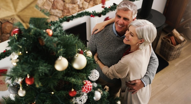 Liebe und Zusammengehörigkeit sind die perfekten Zutaten für ein großartiges Weihnachtsfoto eines glücklichen Seniorenpaares, das zu Hause seinen Weihnachtsbaum schmückt