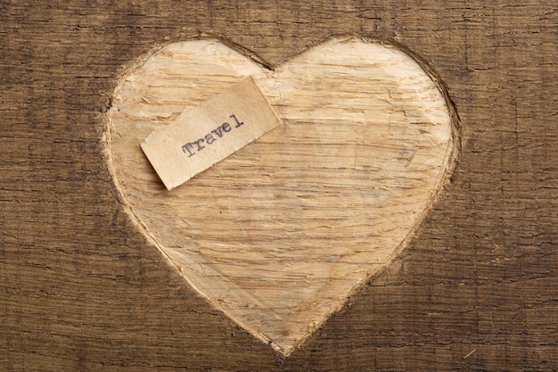 Liebe zum Reisekonzept Reisen Sie mit winzigen getippten Textnotizen, Nahaufnahme geschnitzter Herzform auf Holz als Hintergrund
