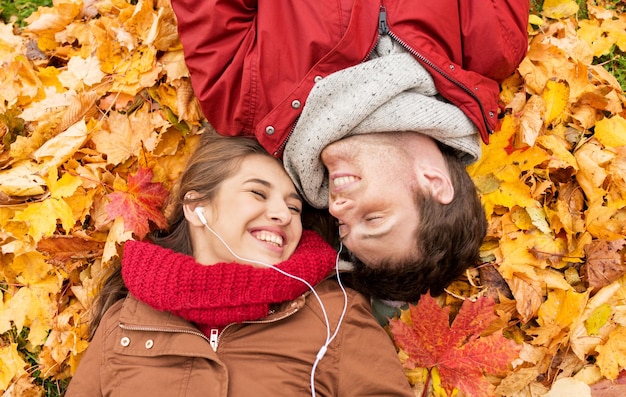 Liebes-, Beziehungs-, Jahreszeiten-, Familien- und Menschenkonzept - Nahaufnahme eines glücklichen Paares mit Kopfhörern, das Musik hört und auf Herbstblättern liegt