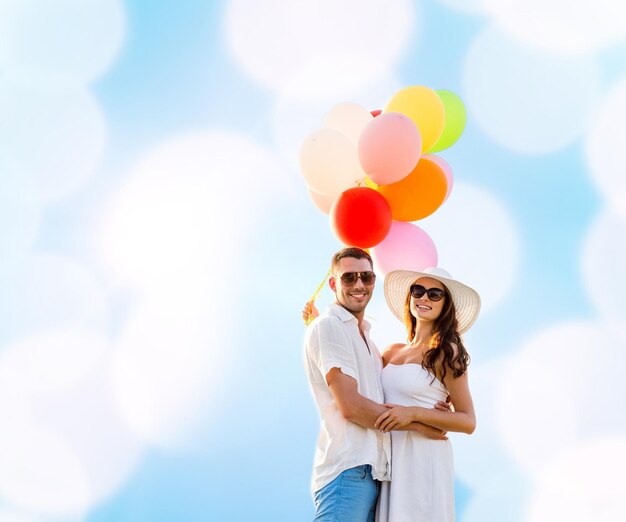 Liebes-, Hochzeits-, Sommer-, Dating- und People-Konzept - lächelndes Paar mit Sonnenbrille und Luftballons, die sich über blauem Hintergrund umarmen