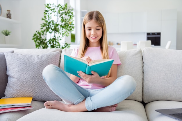 Liebes tagebuch. foto in voller länge von positiven kindermädchen sitzen divanbeine gekreuzt schreibaufgabe im kopierbuch bleistift tragen t-shirt denim-jeans im haus drinnen zimmer