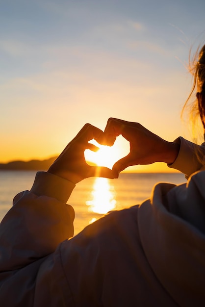 Liebes- und Freedon-Konzept Frau Hände machen Herzform über Sonnenaufgang Himmelshintergrund