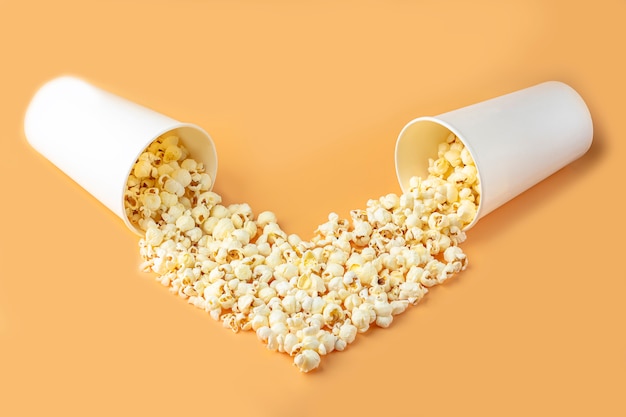 Liebesfilme Konzept. Popcorn in Papierbox verstreut auf orange Hintergrund Hintergrund herzförmige Draufsicht, kopieren Raum für Text. Kino-Snack-Konzept. Popcorn Box Mocap