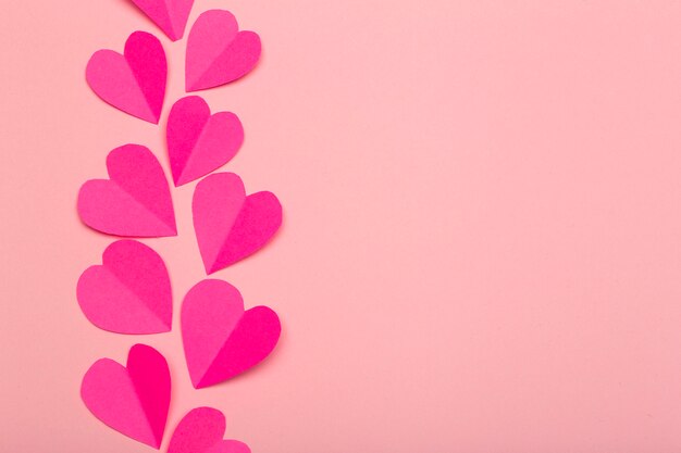 Liebeshintergrund (Valentinstag) oder Hochzeitshintergrund. Rosa Papierherzen auf einem rosa Pastellhintergrund. Liebeskonzept
