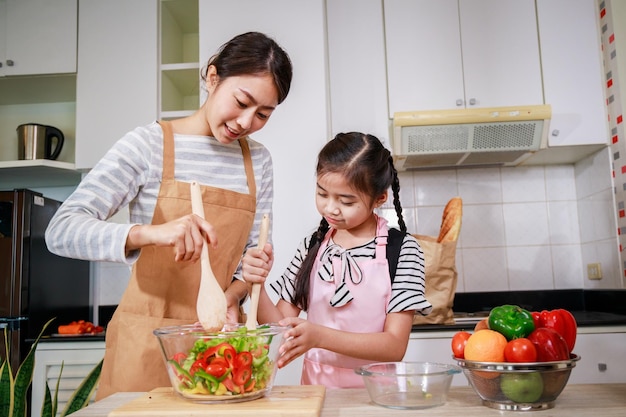 Liebesmoment der asiatischen Familienmutter und -tochter, die helfen, Gemüsesalat in der Küche zu Hause zuzubereiten