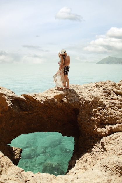 Liebespaar, das Flitterwochen auf Felsen mit luxuriösem Blick genießt und Emotionen auf azurblauem Meereshintergrund zeigt. Glückliche Liebhaber auf romantischer Reise haben Spaß im Sommerurlaub. Konzept Romantik und Entspannung