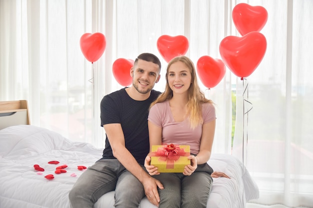 Liebespaar, das Geschenkbox im Schlafzimmerglück in der Liebe Valentinstagkonzept gibt