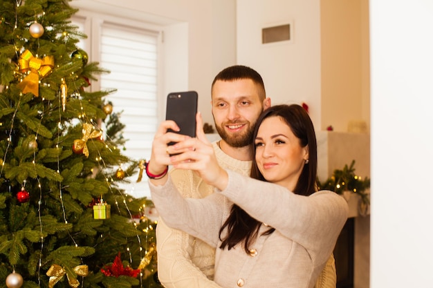 Liebespaar, das sich in der Nähe des weihnachtlich dekorierten Kamins und des Weihnachtsbaums selbst macht. Heiligabend zusammen feiern, Freundschaft