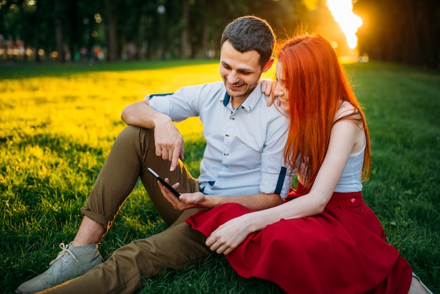 Liebespaar glücklich zusammen, romantisches Datum im Sommerpark auf Sonnenuntergang. Attraktive Frau und junger Mann Freizeit auf einem Gras