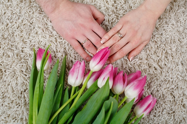 Liebespaar hält sanft die Hände in der Nähe. Hochzeitstag. Liebesgeschichte Konzept. bräutigam sanft hält die hand braut. zwei Hände mit Eheringen und Strauß Tulpen.