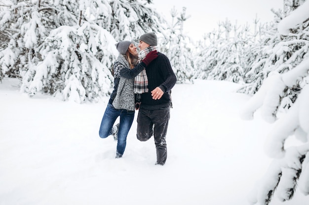 Liebespaar läuft im Winter in einem Pullover und einem Schal durch einen verschneiten Wald und lächelt