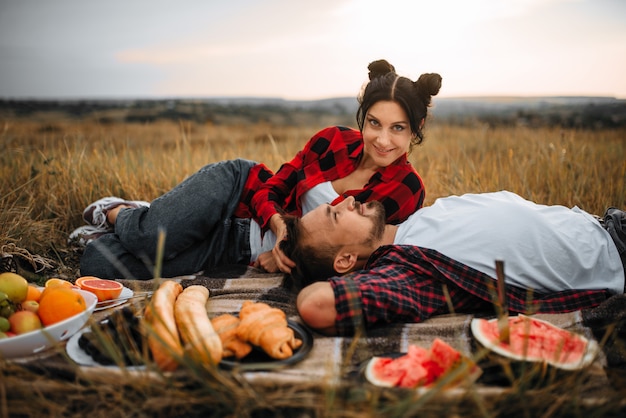 Liebespaar liegt auf kariertem Fruchtpicknick im Sommerfeld. Romantisches Junket von Mann und Frau