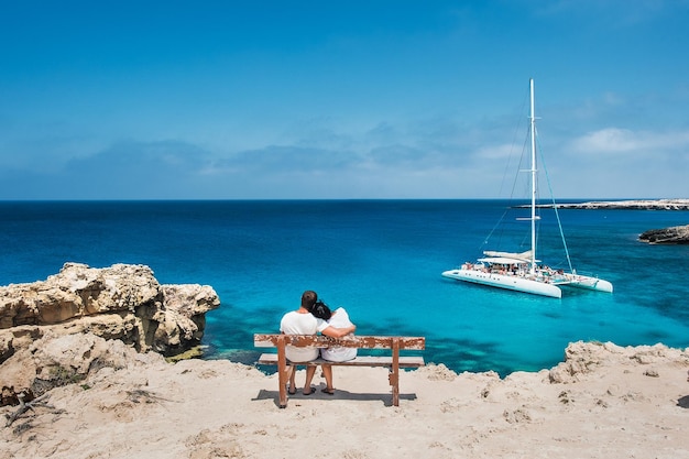 Liebespaar sitzt auf einer Bank und schaut auf die Lagune. Flitterwochen-Liebhaber. Mann und Frau auf der Insel. Verliebtes Paar im Urlaub. Ein Gutschein für eine Kreuzfahrt. Meerestour. Flitterwochen. Kreuzfahrtschiff