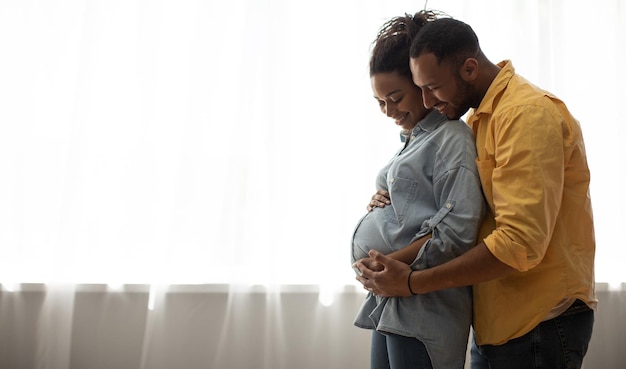 Liebevolle afroamerikanische Ehepartner umarmen sich zu Hause in der Nähe des Fensters