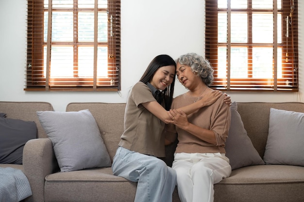 Liebevolle erwachsene Tochter, die ältere Mutter umarmt, die zu Hause hinter der Couch steht, Familie, die einen zärtlichen Moment zusammen genießt