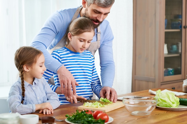 Liebevolle Familie, die Gemüsesalat zubereitet