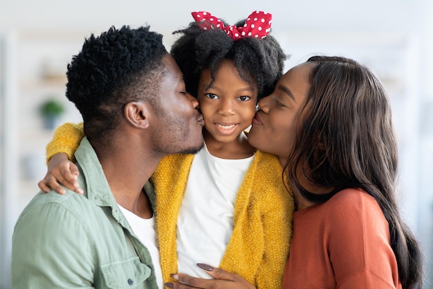 Liebevolle Familie, glückliche afroamerikanische Eltern, die ihre süße kleine Tochter küssen