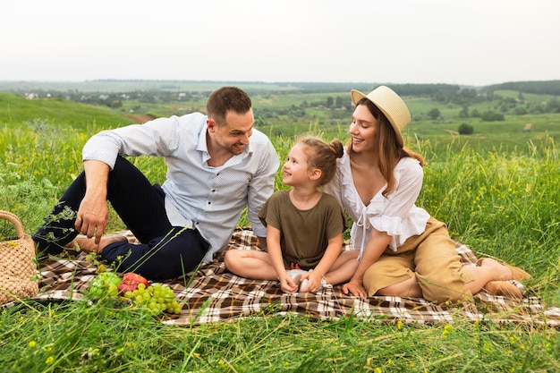 Liebevolle Familie mit einem entzückenden Kind, das das Wochenende zusammen beim Picknick auf der Wiese verbringt und sich ansieht