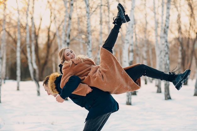 Liebevolle junge Paare, die im Winterwaldpark spazieren gehen und Spaß haben