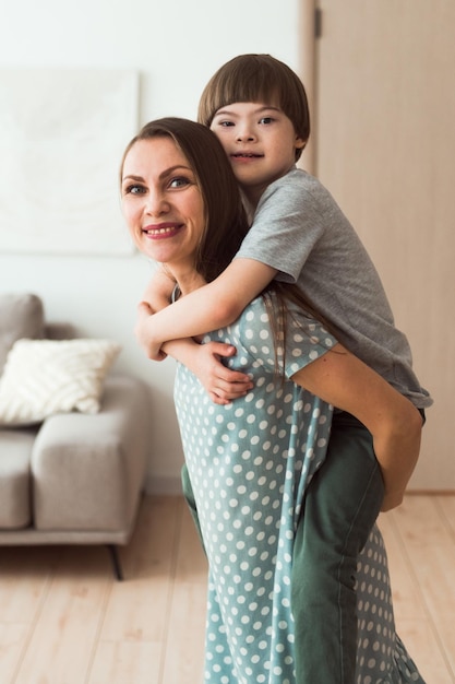 Liebevolle Mutter, die Huckepackjungen mit Down-Syndrom hält