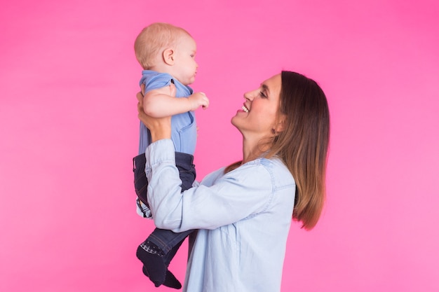 Liebevolle Mutter, die mit ihrem Baby auf rosa Hintergrund spielt