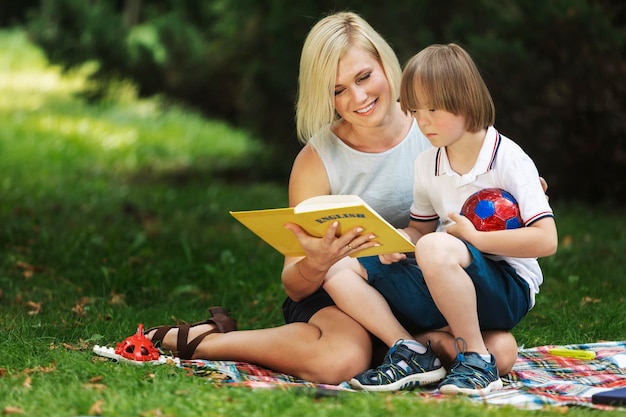 Liebevolle Mutter liest ihrem besonderen Kind auf einer Parkwiese ein Buch vor