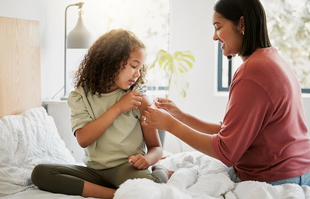 Liebevolle Mutter tröstet ihre Tochter mit einem Bandaid im Bett, das zu Hause liebevoll und fürsorglich ist Junge Eltern helfen ihrem kranken Kind beim Anbringen eines Pflasters und verbinden besondere Momente der Mutterschaft