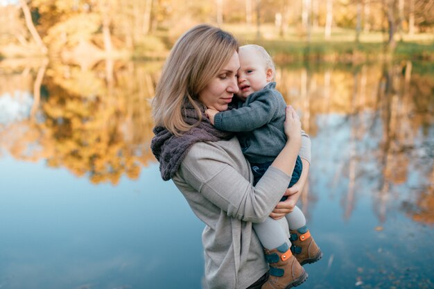 Liebevolle Mutter umarmt ihr schläfriges Kind in der Natur mit See