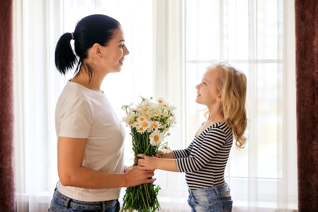 Liebevolle mutter und kleine tochter zu hause mit einem strauß gänseblümchen. die familie hat eine gute zeit zusammen.