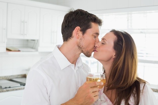 Liebevolle Paare, die in der Hand mit Weinglas in der Küche küssen
