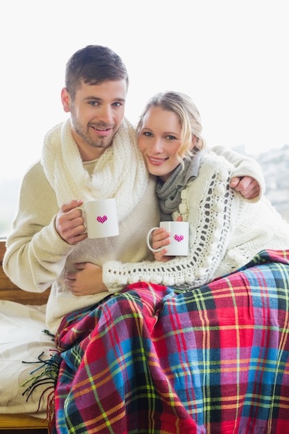 Liebevolle Paare in der Winterkleidung mit Kaffeetassen gegen Fenster