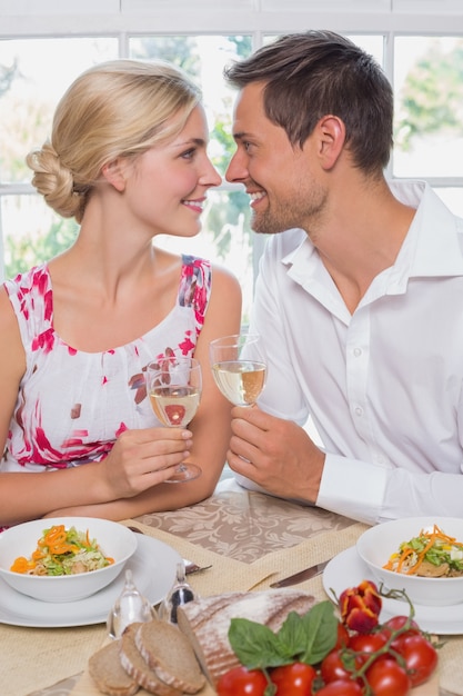 Liebevolle Paare mit den Weingläsern, die einander an Speisetische betrachten