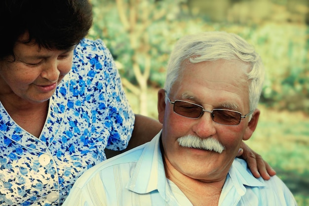 Liebevolle reife Umarmungen an einem Sommertag im ParkSenior-Paare sitzen im FreienEine ältere Frau umarmt einen alten Mann