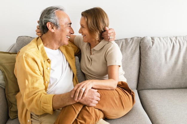 Liebevolle verheiratete ältere Ehepartner umarmen sich, schauen sich an und lächeln, ruhen sich zu Hause kostenlos auf dem Sofa aus