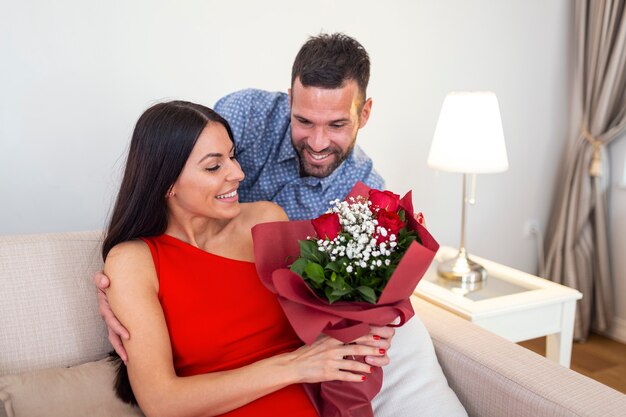 Liebevoller junger Mann, der seiner schönen jungen Frau am Valentinstag einen Strauß roter Rosen schenkt