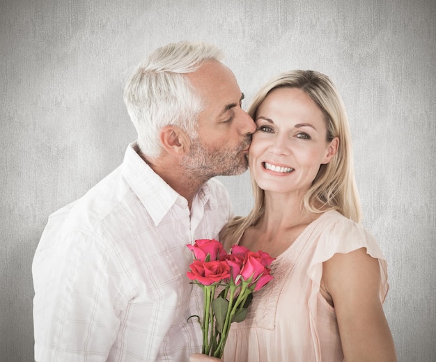 Liebevoller Mann küsst seine Frau auf die Wange mit Rosen gegen verwitterte Oberfläche