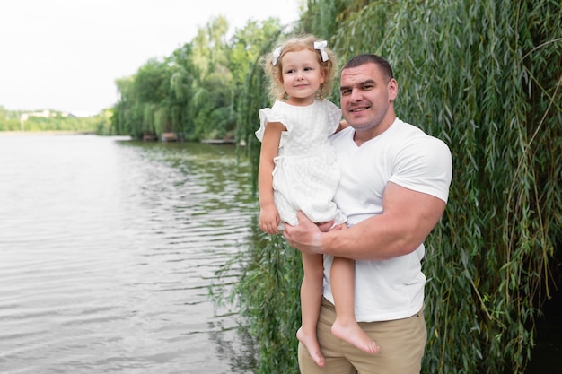 Liebevoller muskulöser Bodybuilder-Vater mit kleiner Tochter steht auf der Brücke in der Nähe des Flusses Vati und Dau