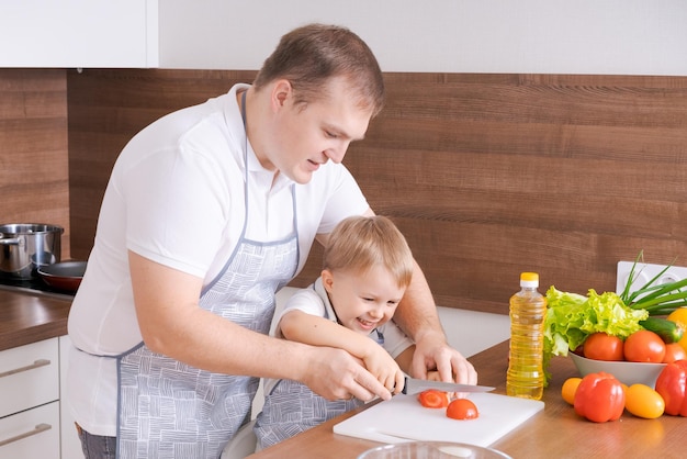 Liebevoller Vater und kleiner Sohn im Vorschulalter, der geschnittenes Gemüse für Salat kocht