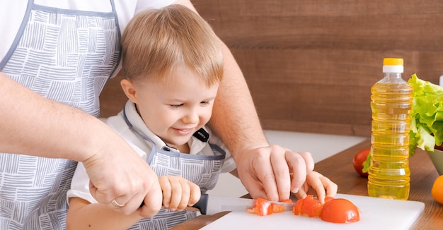 Liebevoller Vater und kleiner Sohn im Vorschulalter, der geschnittenes Gemüse für Salat kocht