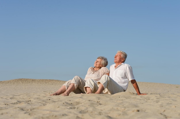 Liebevolles älteres Paar, das sich im Sommer auf dem Sand ausruht