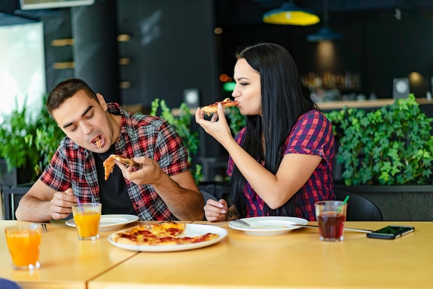 Liebevolles junges Paar bei einem Date in einem Café, das leckere Pizza isst Ein glücklich lächelndes Paar, das Pizza isst und eine tolle Zeit hat