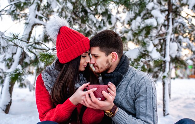 Liebevolles junges Paar, das in einem verschneiten Wald ruht. Umarmen und küssen. Urlaubskonzept