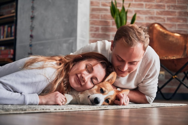 Liebevolles junges Paar, das mit süßem Hund auf dem Boden liegt