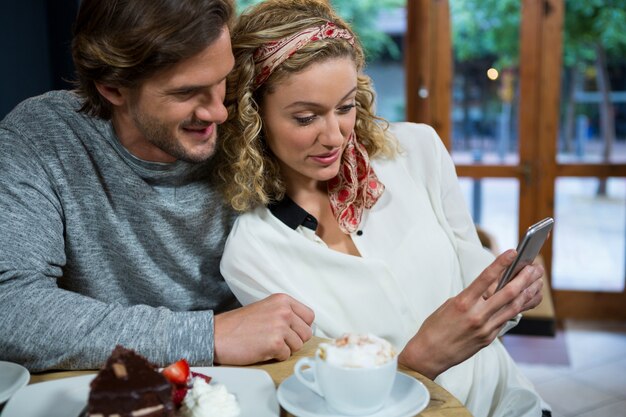 Liebevolles junges Paar mit Smartphone am Tisch in der Cafeteria